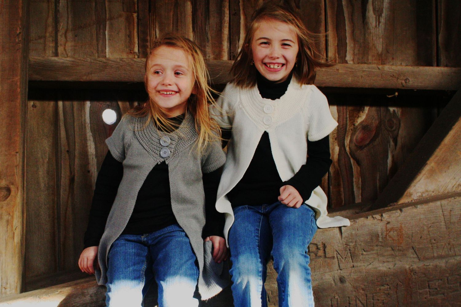 two girls sitting inside a covered bridge, laughing