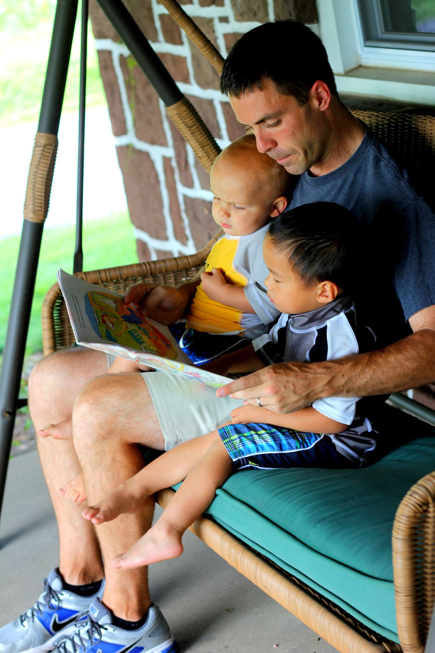 a father reading two his two sons on a porch swing