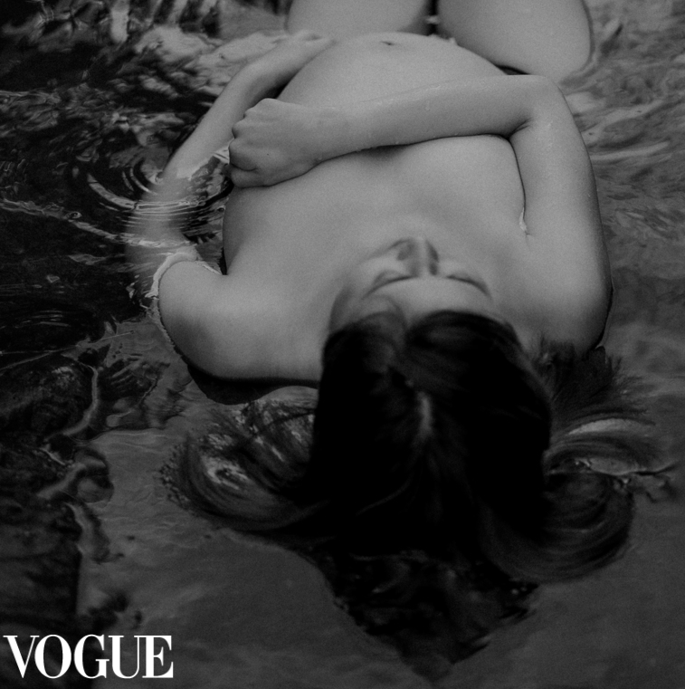 Artistic black and white photo of a figure floating in dark water with Vogue branding.
