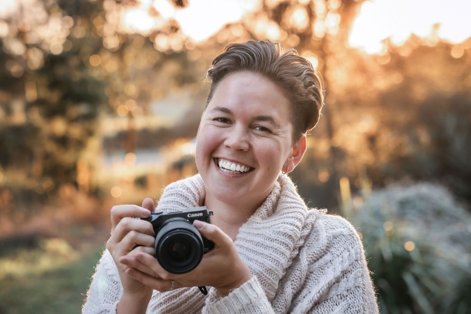 Person in cream sweater holding camera during golden sunset photography session.