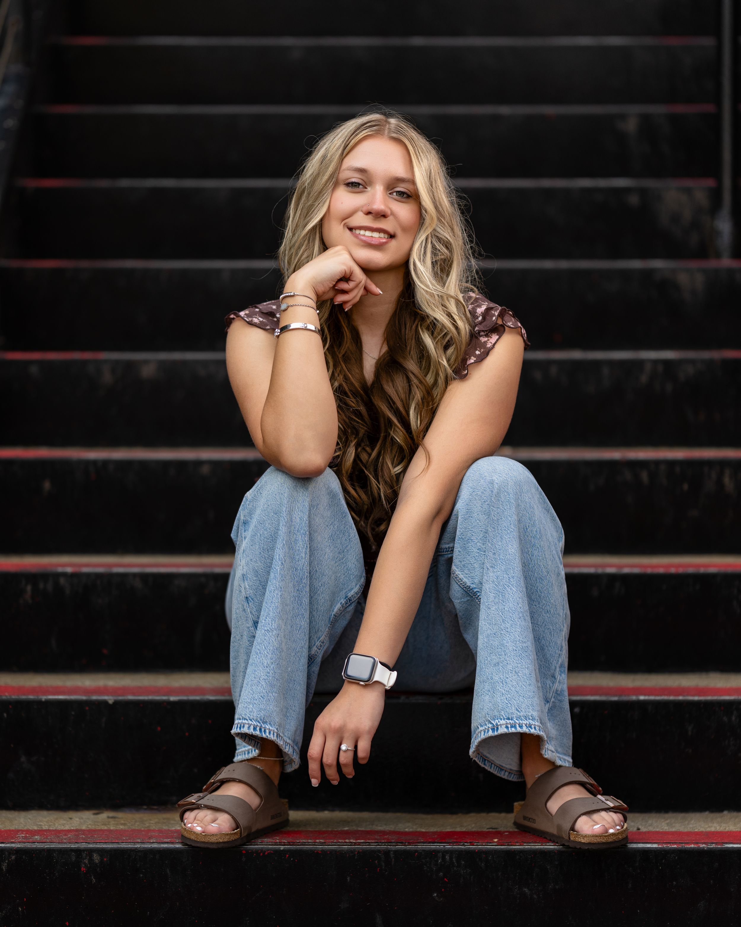 A person in jeans sits casually on red bleacher steps while smiling and posing for a series of candid shots.