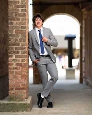 A person in a gray suit and blue tie strikes playful poses in a brick archway corridor.