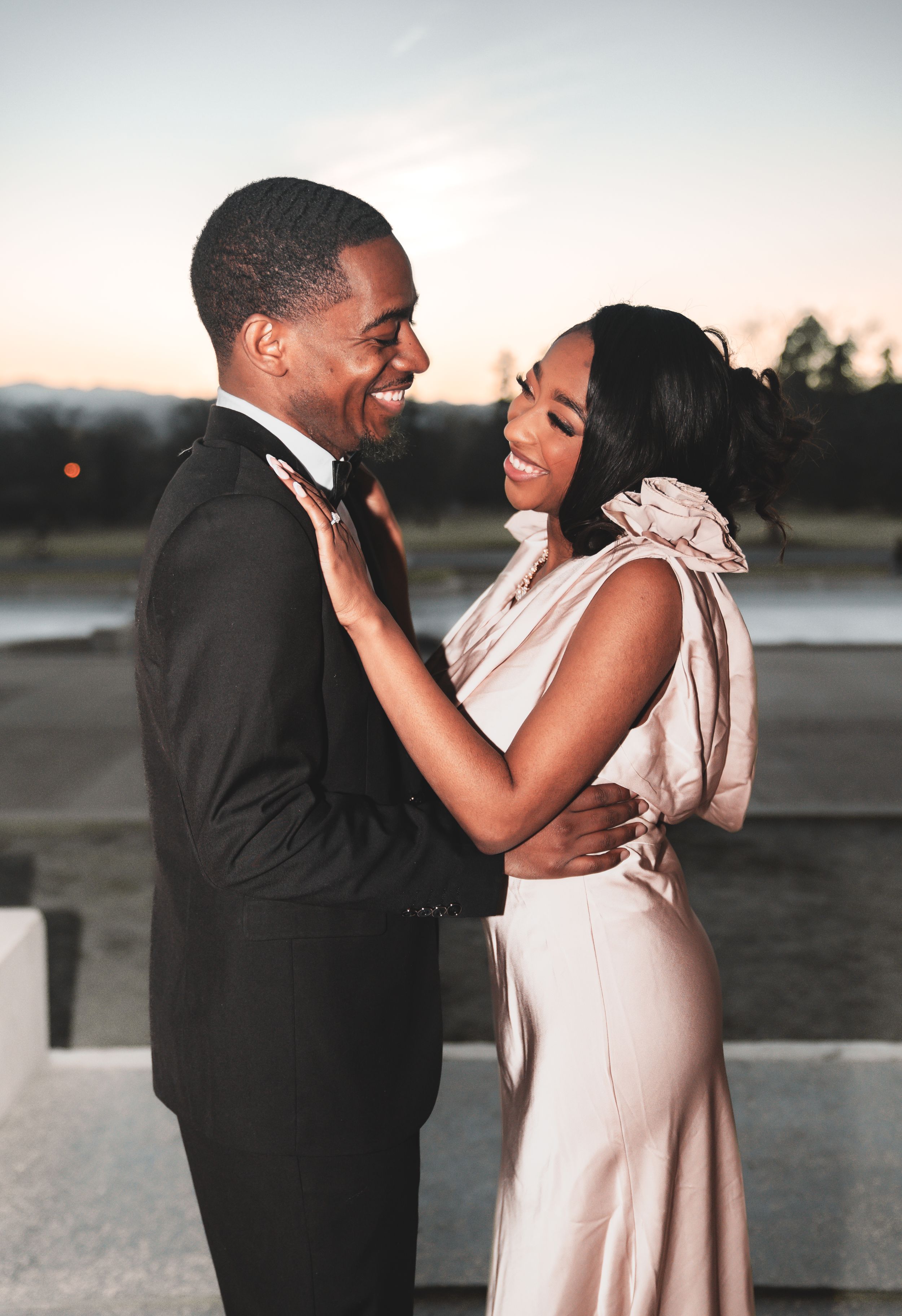 A romantic couple shares joyful moments during their sunset photoshoot wearing formal attire in black and beige.