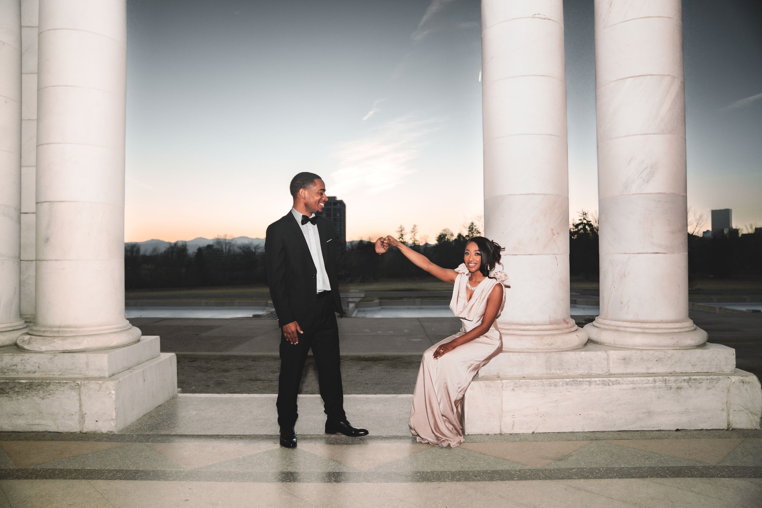 Elegant couple poses for romantic wedding photos between white classical columns at sunset.