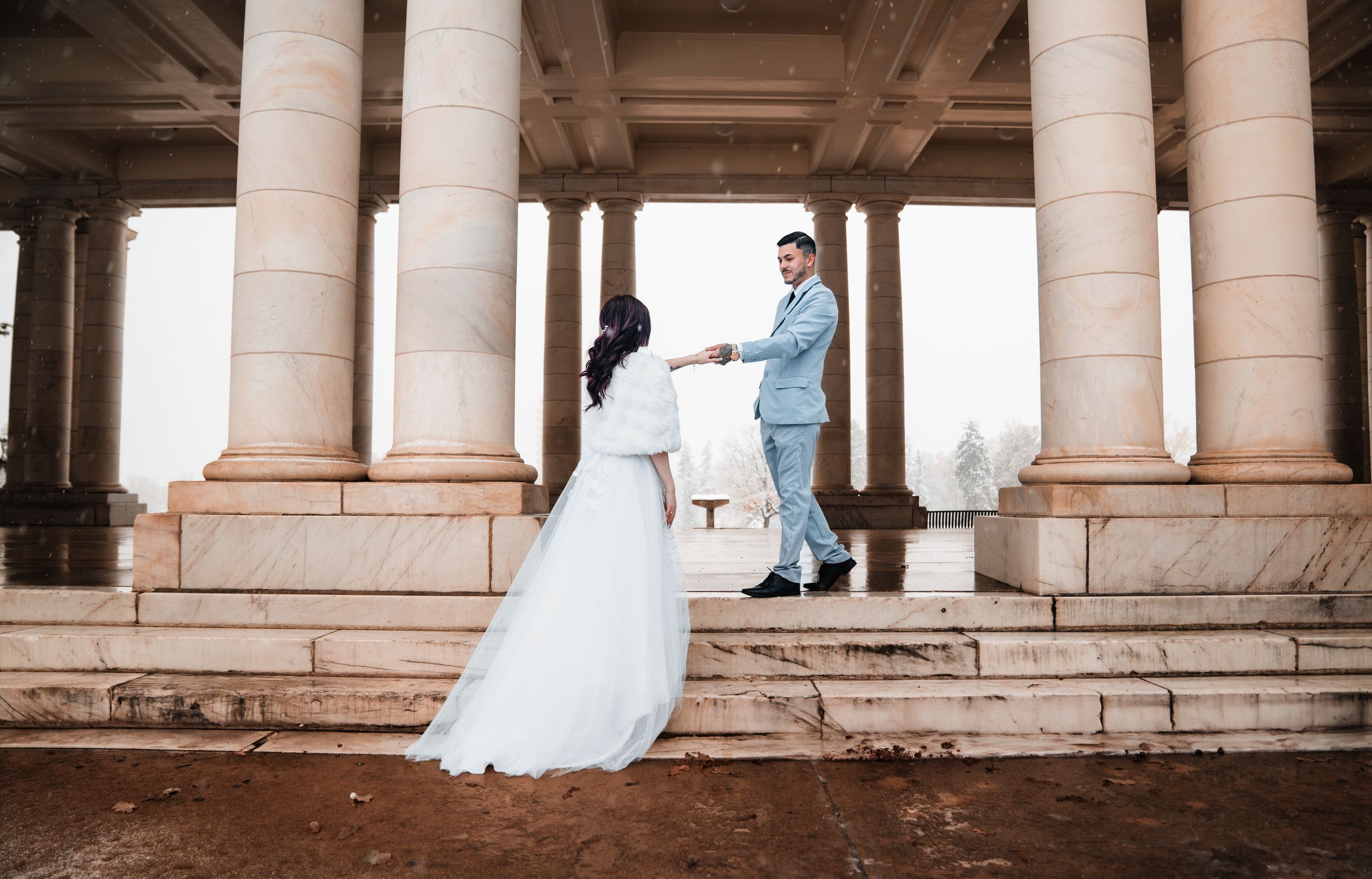 A bride and groom pose under a grand columned archway during their wedding photoshoot.