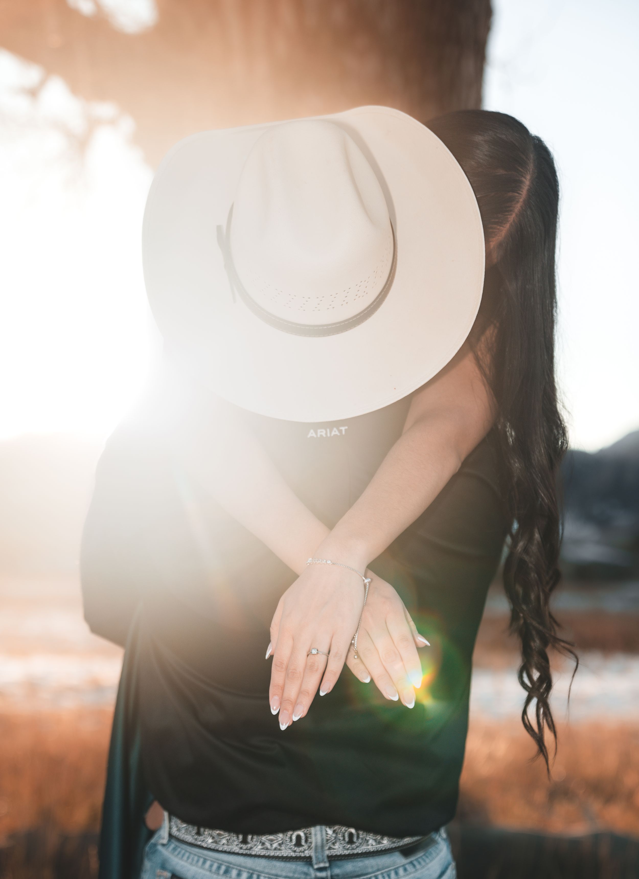 A person wearing a black top poses against a sunlit background with lens flare creating a dreamy atmosphere.