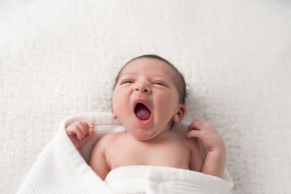 yawning newborn wrapped in white blanket minimalist Halifax studio photography