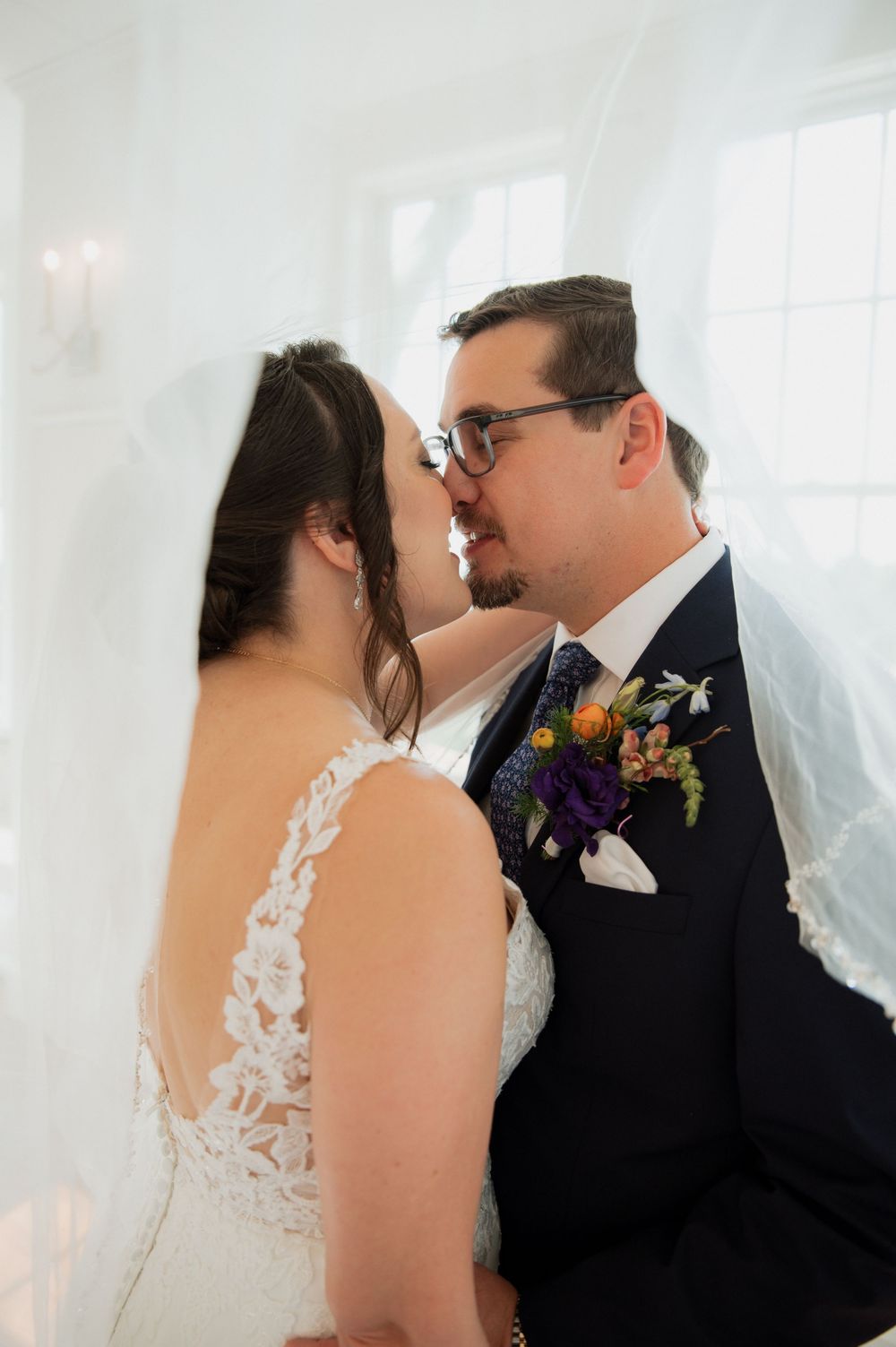 A romantic wedding moment between a bride in lace dress and groom in black suit with colorful boutonniere.
