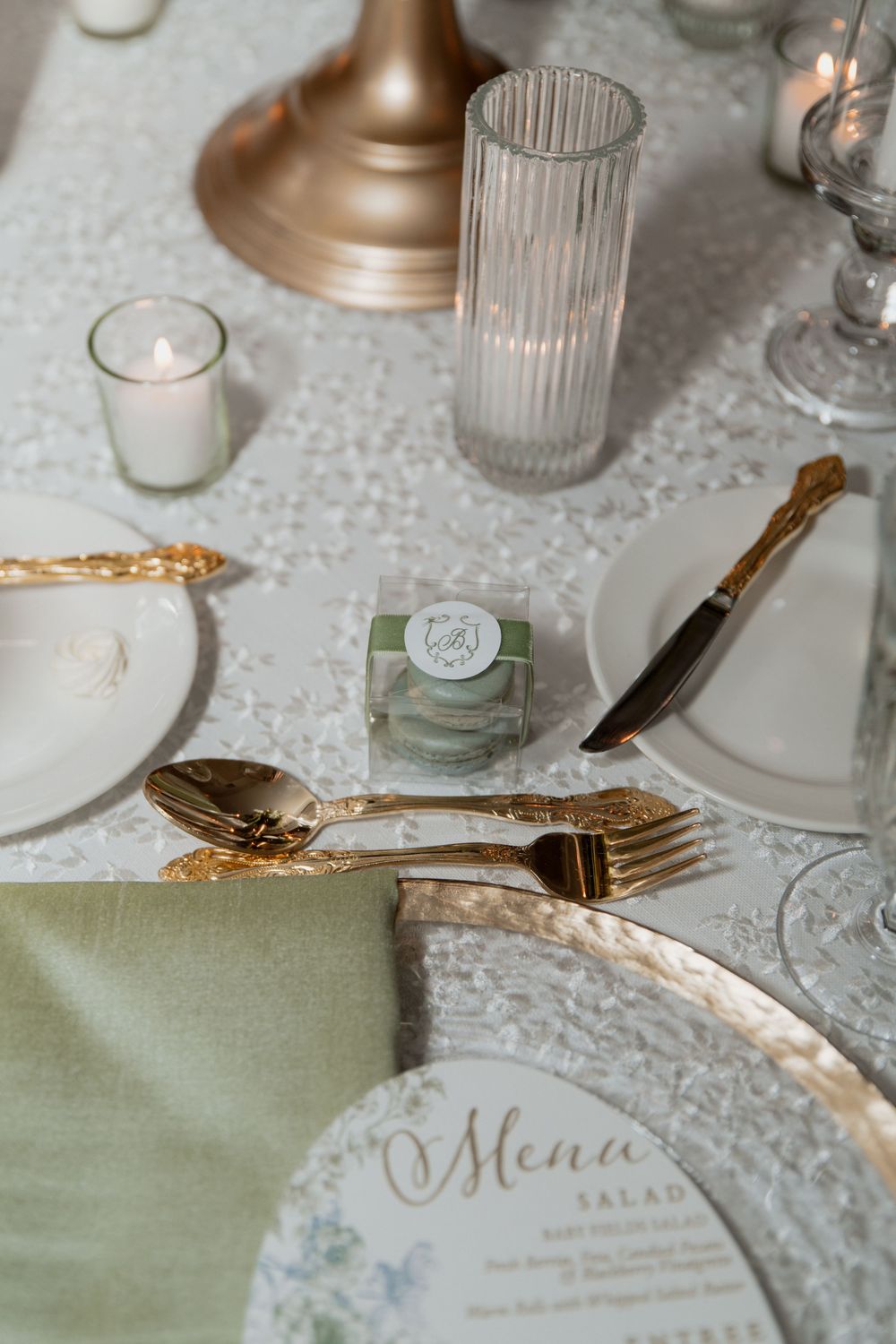 Elegant place setting with sage napkin, crystal glassware, gold flatware, and menu card on textured white tablecloth.