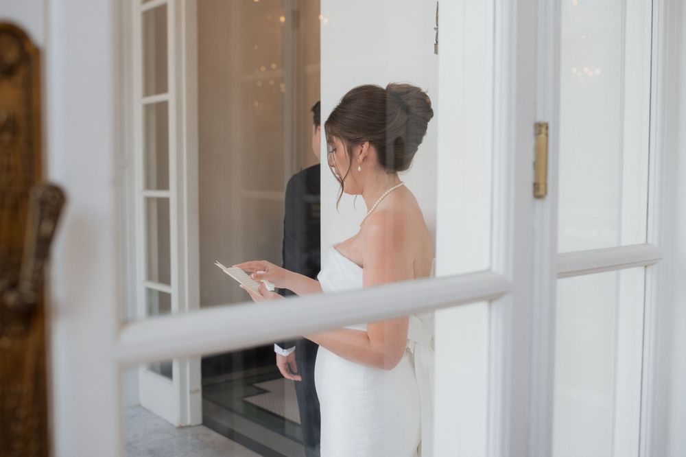 Someone in a white dress checks their phone near white French doors in an elegant interior setting.