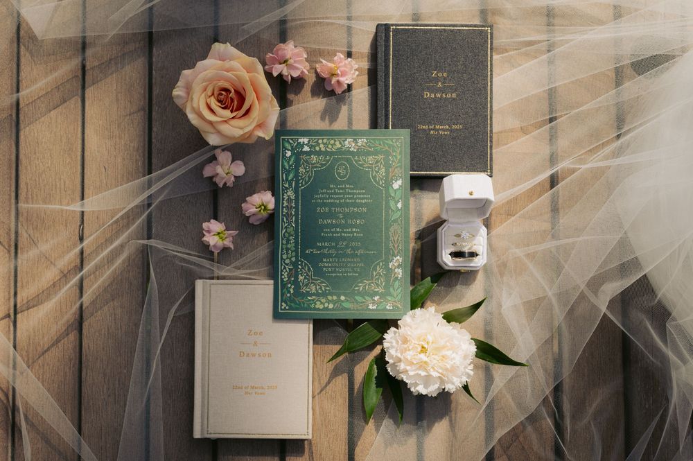 Wedding invitations and decorative items arranged with delicate pink roses and green and white accents.