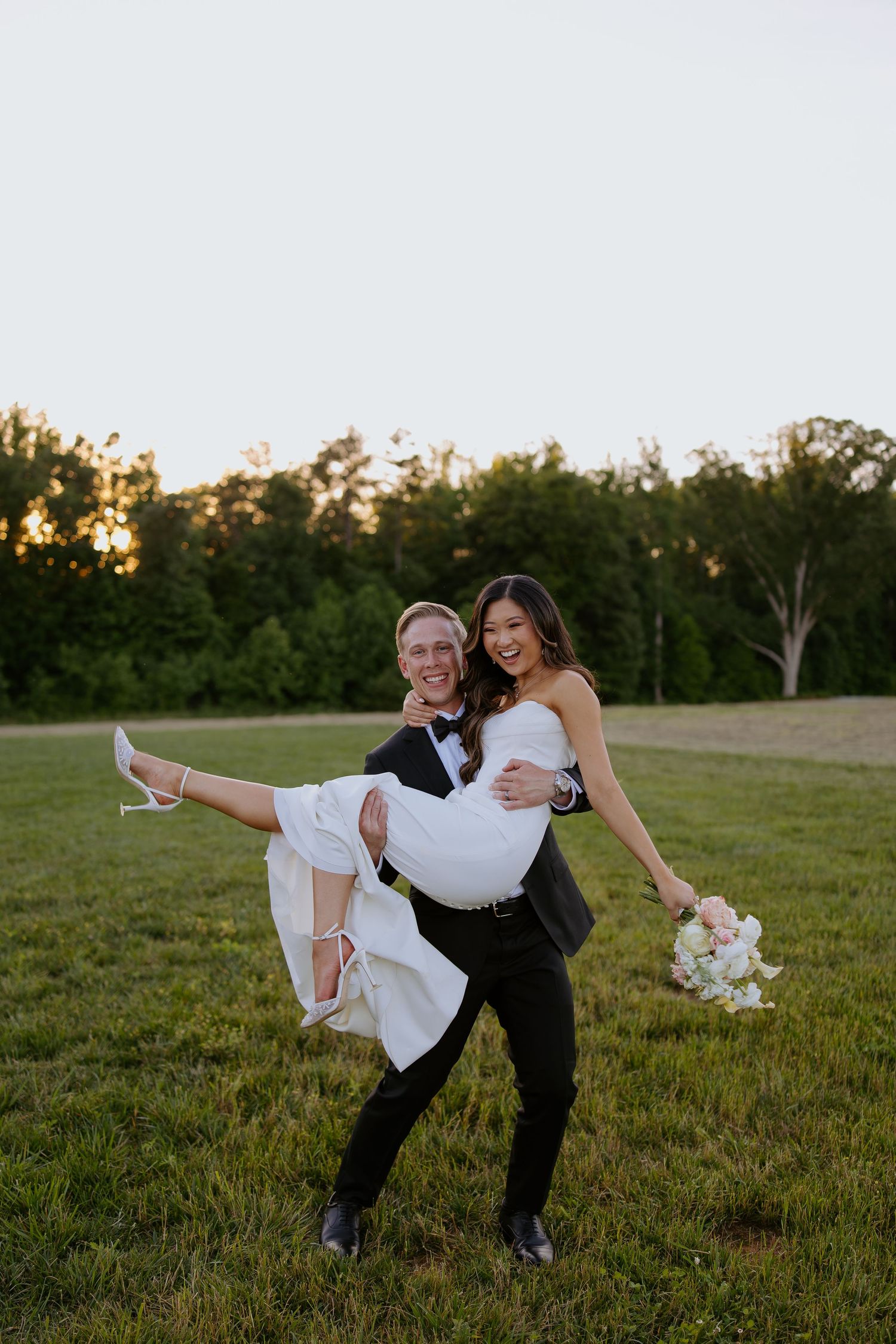 Playful wedding photo with bride being carried in her white dress while holding bouquet.