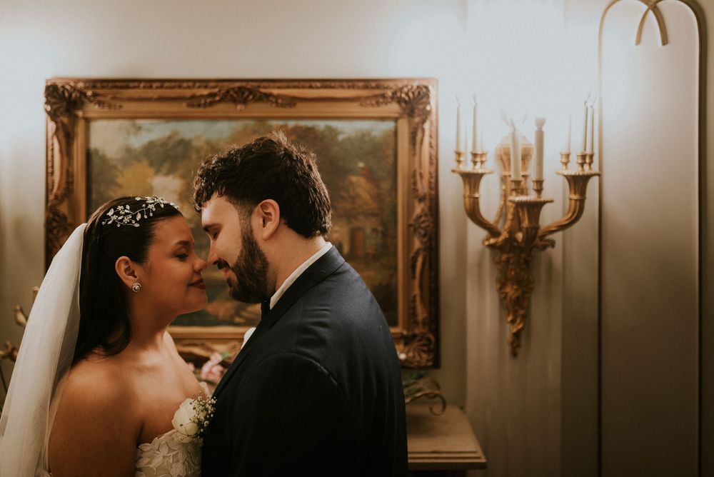 Bride and groom share an intimate moment, forehead to forehead, in a warmly lit room with golden decor.