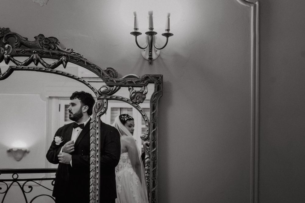 Black and white wedding photo of bride and groom reflected in ornate mirror with candelabra.