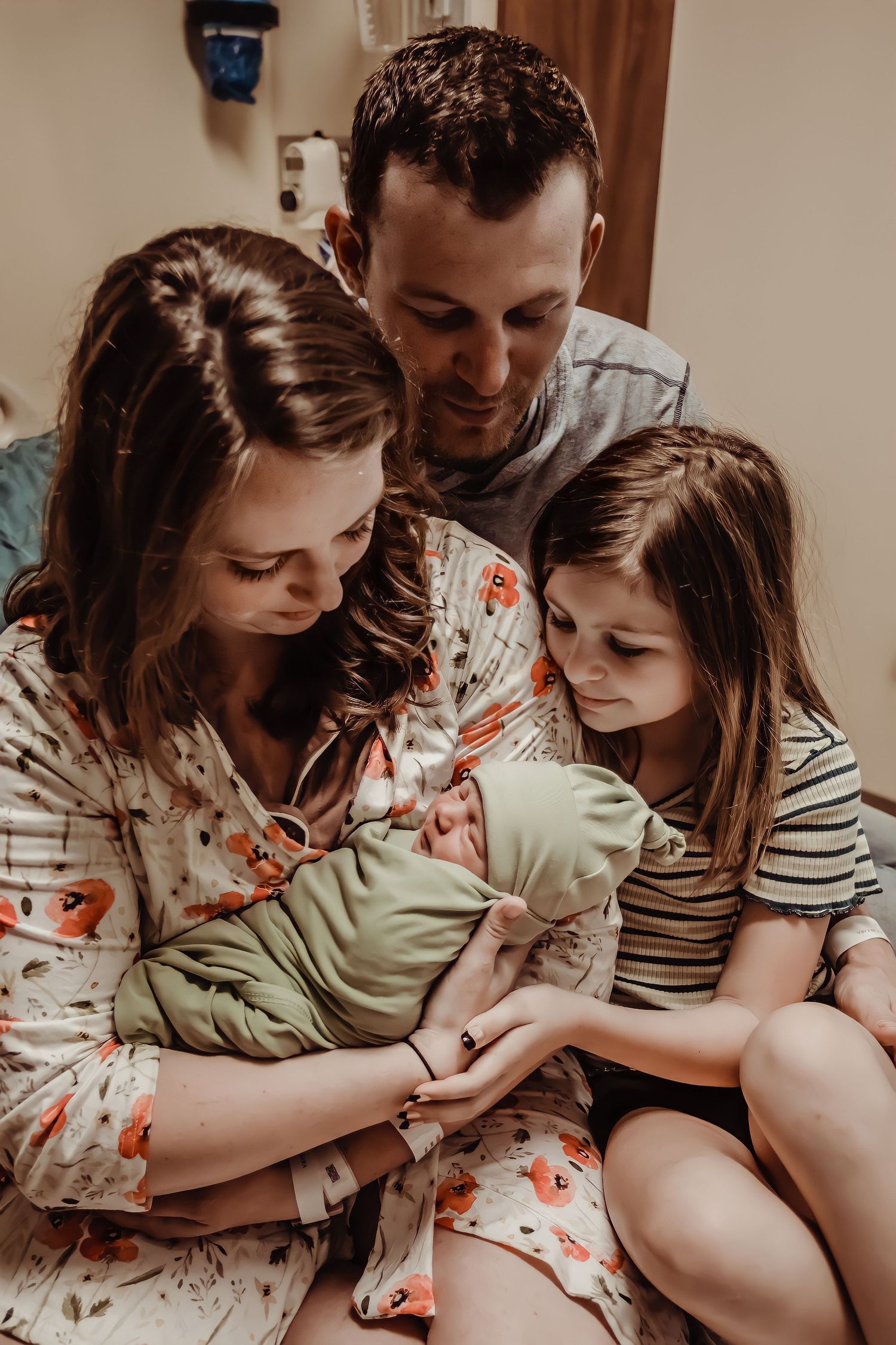Family sharing tender moment while gazing at newborn baby wrapped in mint green blanket.