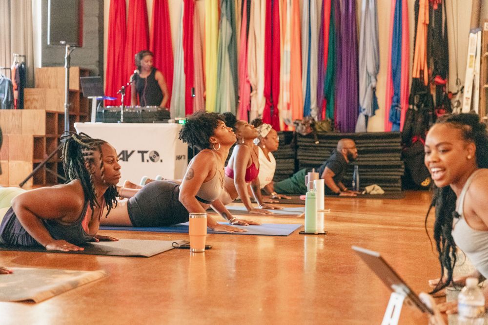 Group of people practicing yoga in a spacious studio with colorful hanging fabrics.