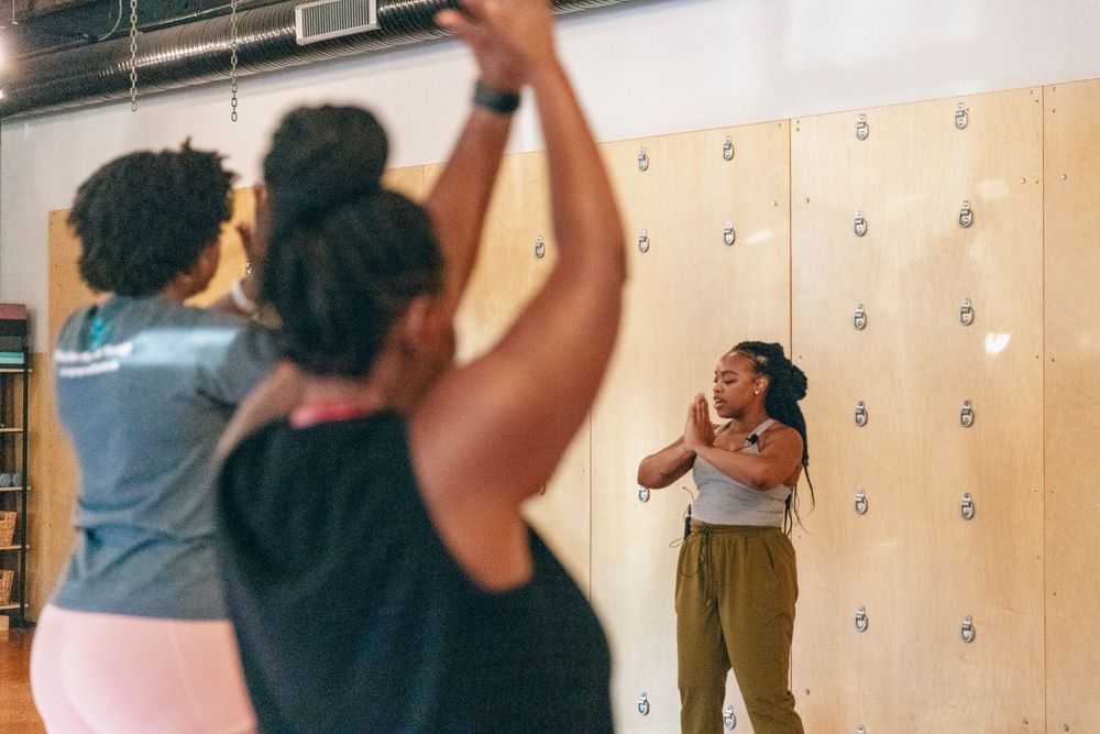 People participate in a fitness or dance class in a gym with lockers visible.