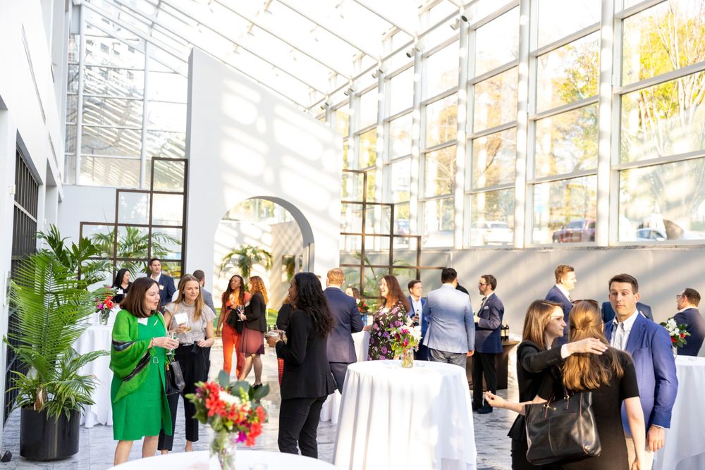 Elegant networking event in a bright atrium with guests mingling around cocktail tables and window views.