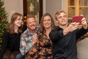 A group taking a selfie together while sitting on a couch during Christmas time with a decorated tree in background.