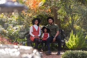 A family poses on a garden bench surrounded by autumn foliage and blooming flowers in a lush outdoor setting.