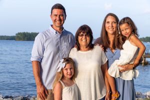 A family of five poses together at sunset by the water's edge on a beautiful summer evening.