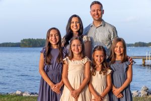 A family poses together by a waterfront during sunset wearing coordinated navy blue and cream colored dresses.