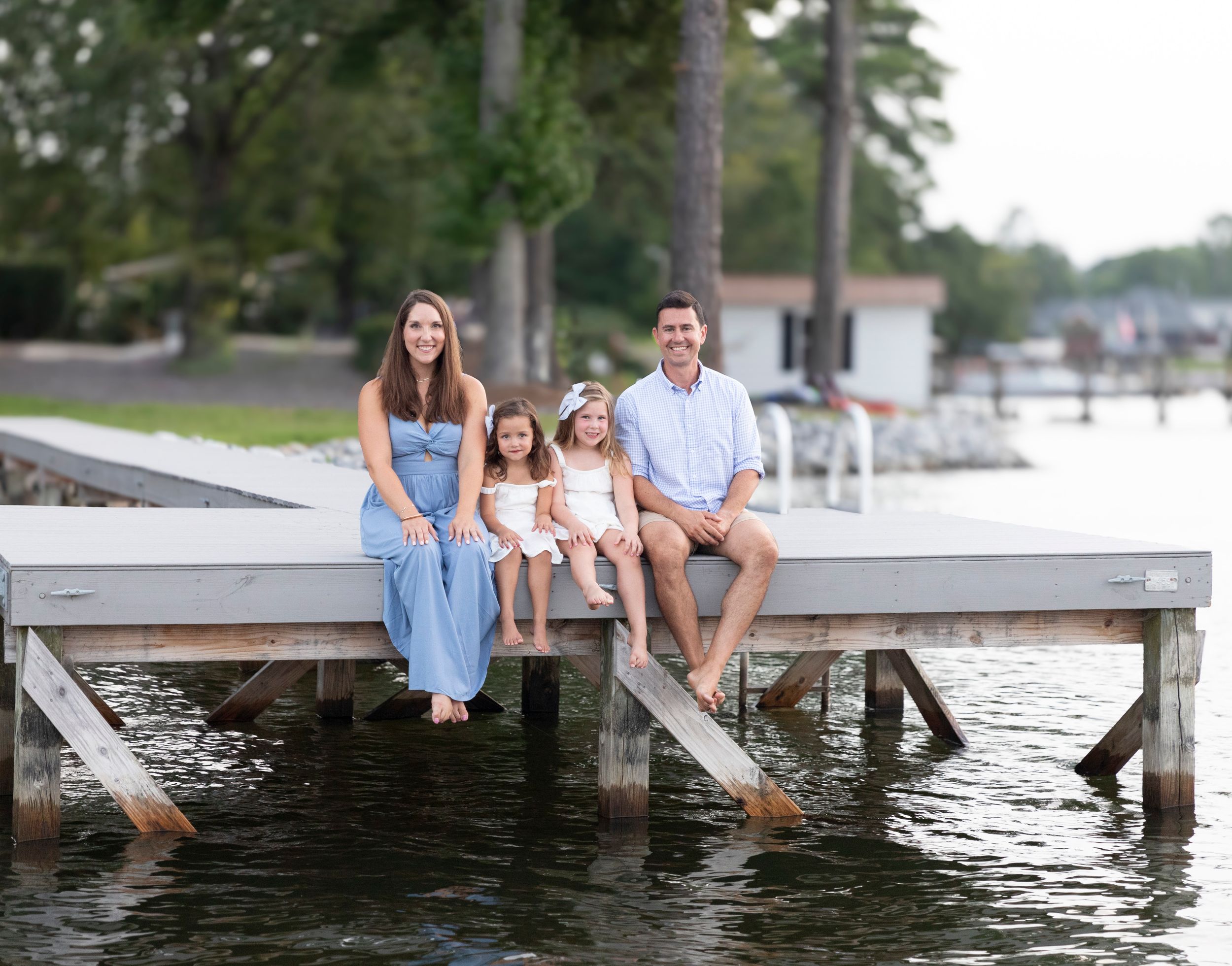A cheerful family sits together on a wooden dock by the lake during a sunny summer day.