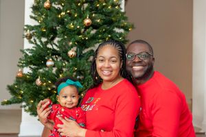 A joyful family wearing coordinated red outfits poses in front of a decorated Christmas tree with ornaments and lights.