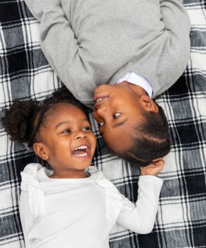 Two children laying on a black and white plaid blanket laugh joyfully together in a candid moment.
