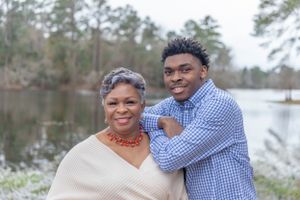 Mother and son pose warmly together outdoors by a peaceful lake with trees in the background.