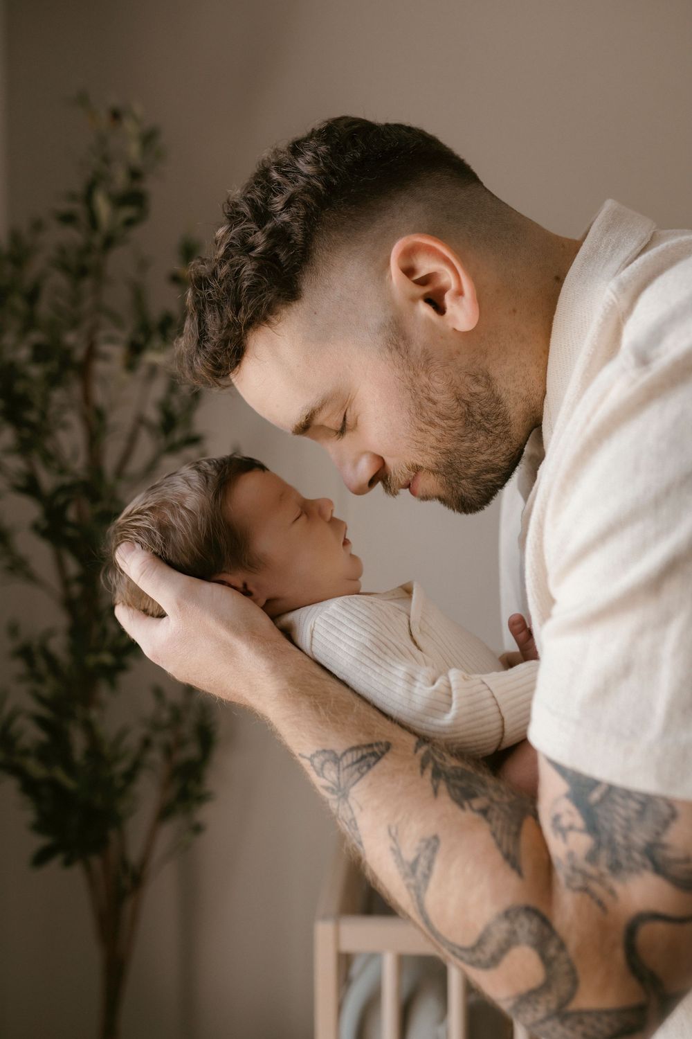 An intimate portrait of parent and baby sharing a gentle forehead touch against a neutral background.