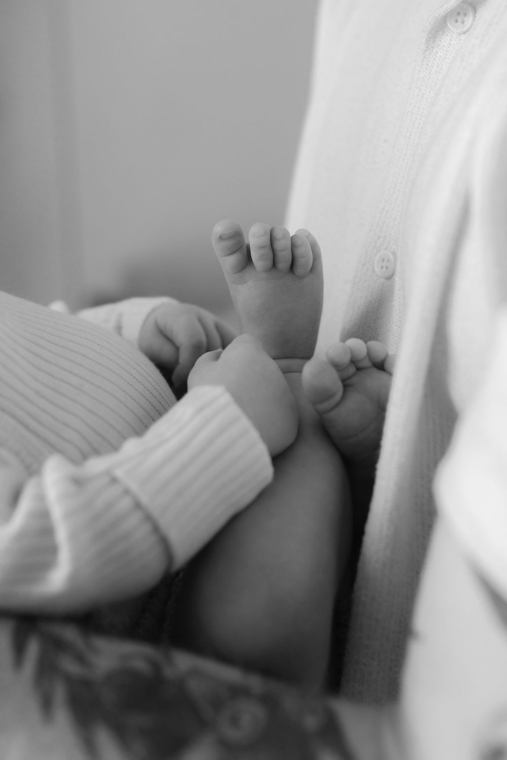 Close-up black and white image of tiny baby feet against white clothing.