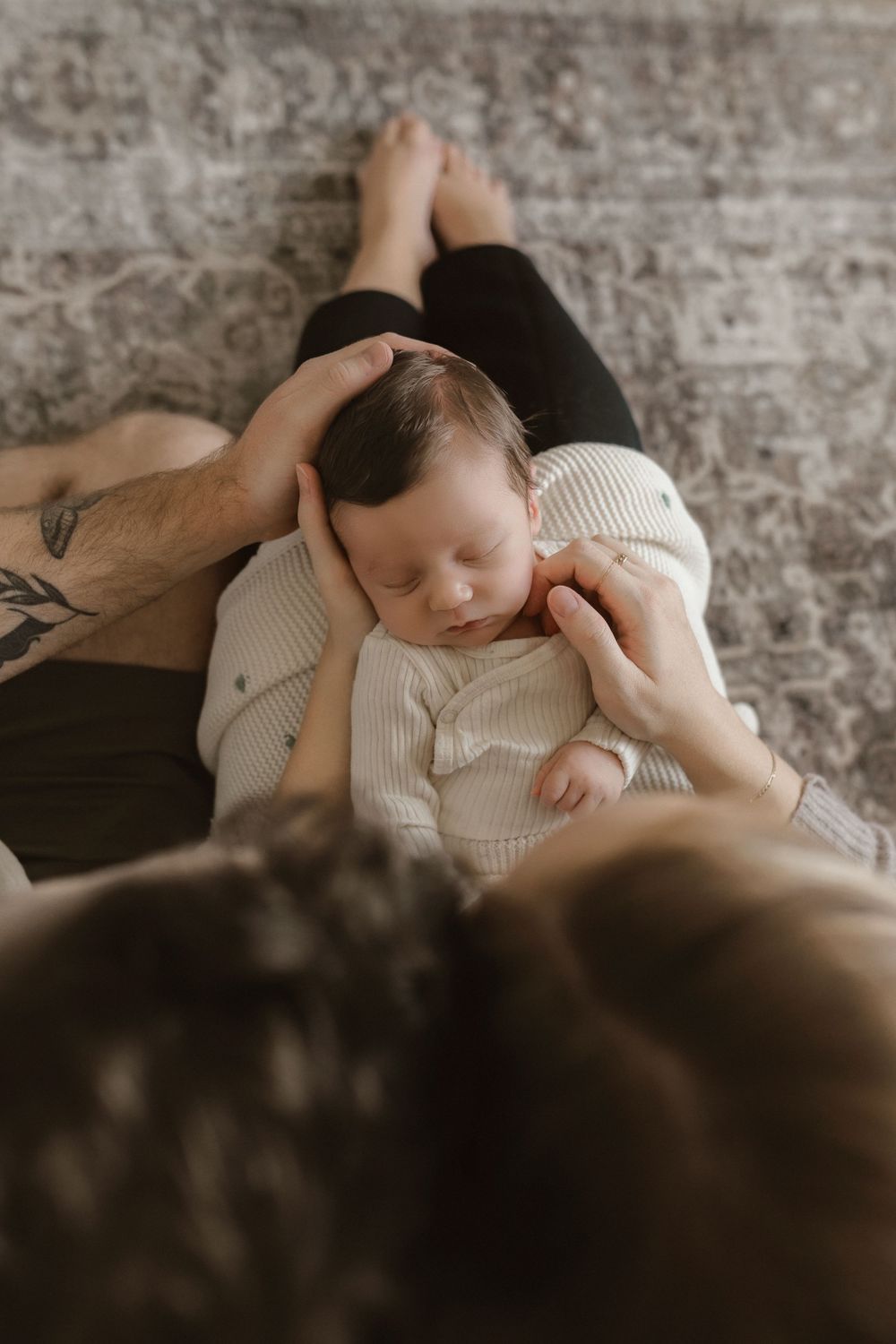 Overhead view of a sleeping baby in a white knit outfit being tenderly held.
