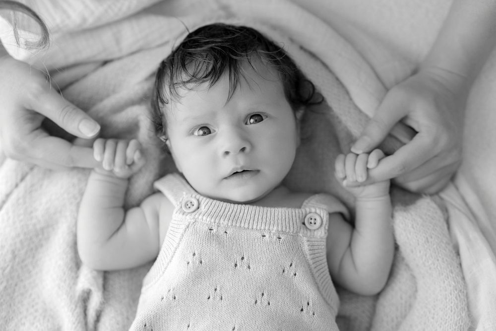 Black and white portrait of baby in white eyelet dress laying on soft blanket.