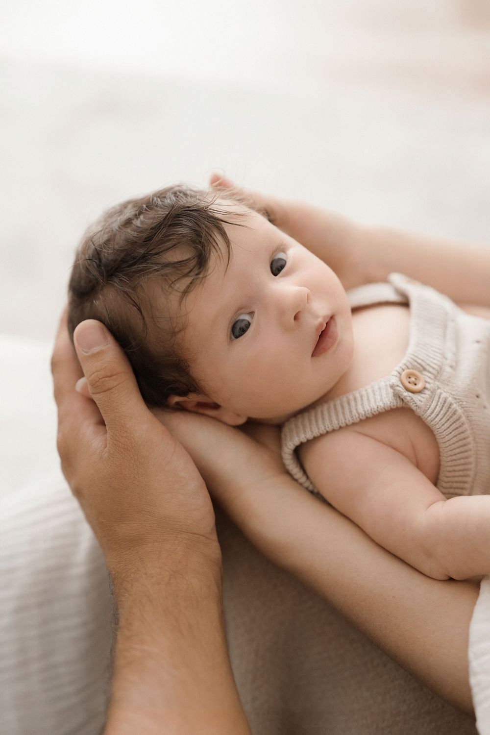 Close-up of baby in cream knit outfit being cradled by gentle hands.