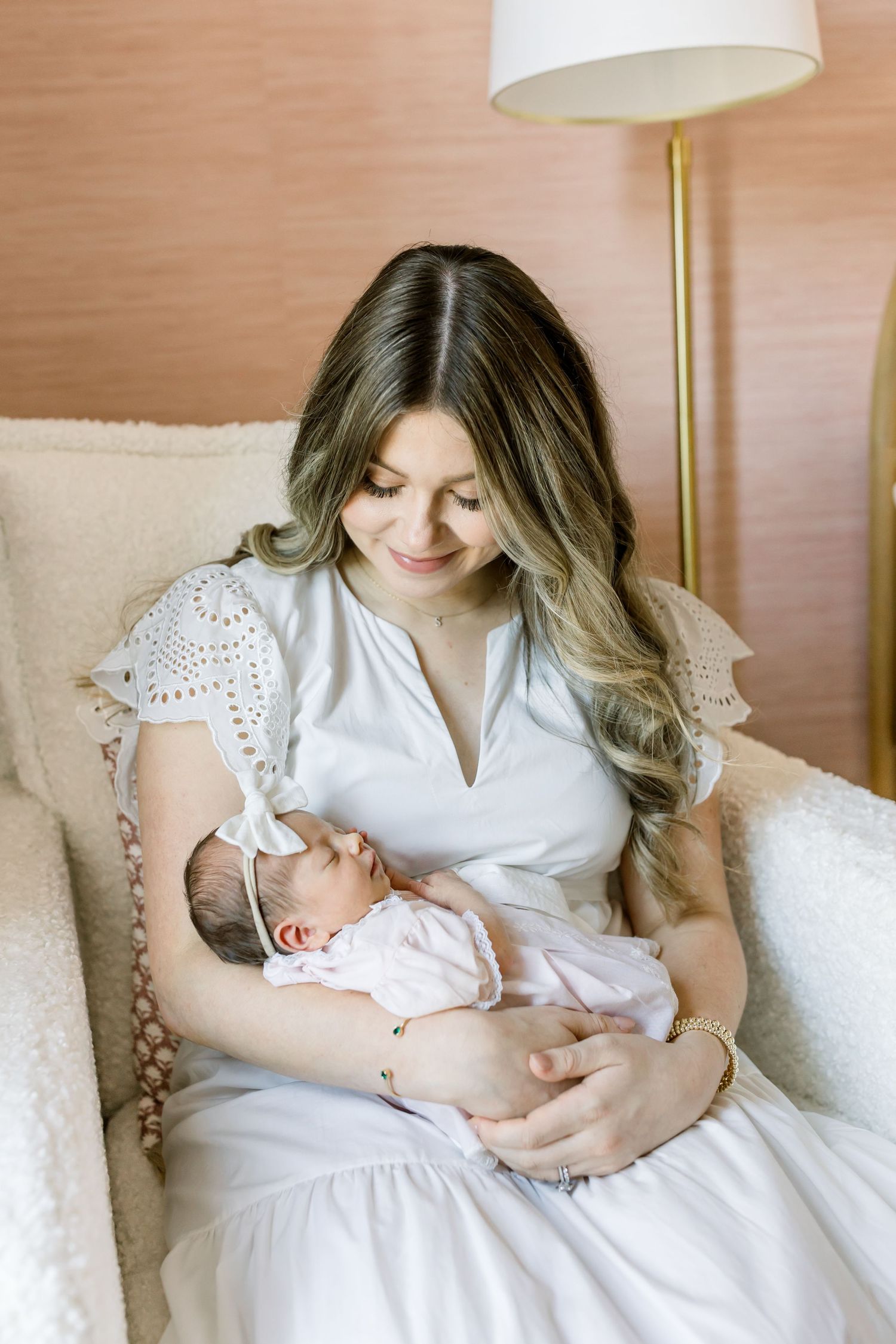 Tender moment in pink nursery with white eyelet dress and soft natural lighting.