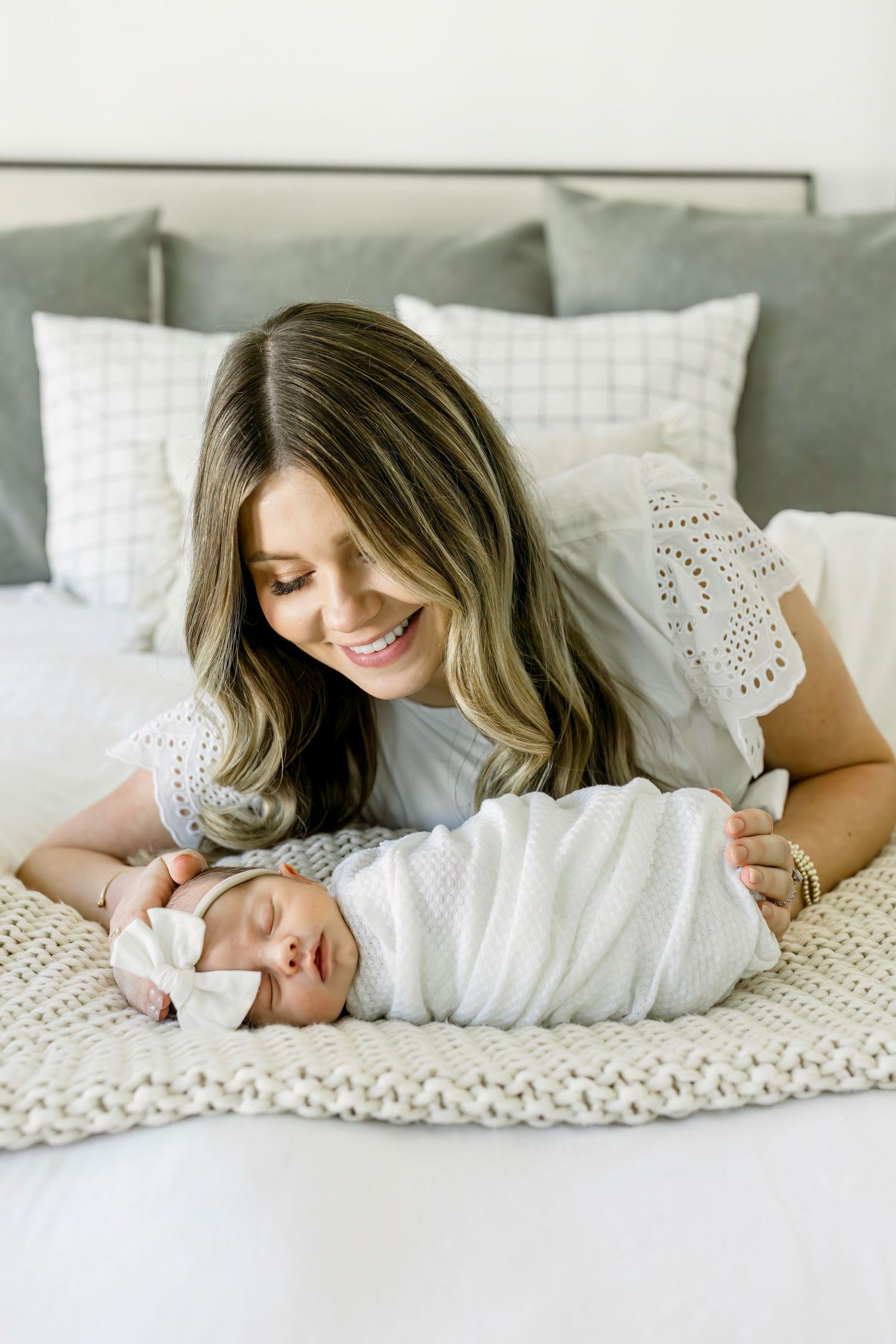 Sleeping newborn in white wrap with parent on knitted blanket.
