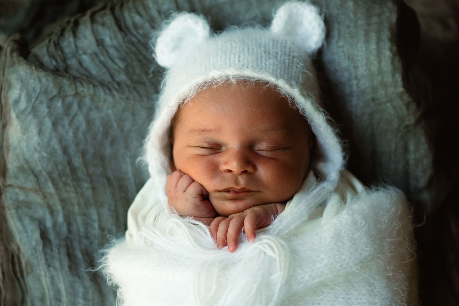 newborn posed in a little bear hat with his face resting on his little fist in newborn photography session