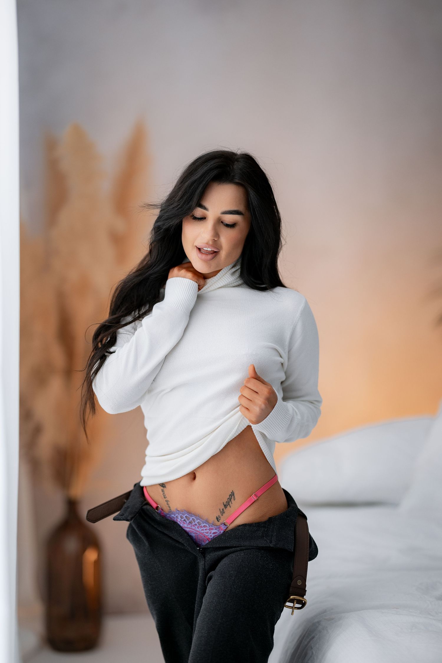 Model in white sweater and jeans poses playfully indoors.