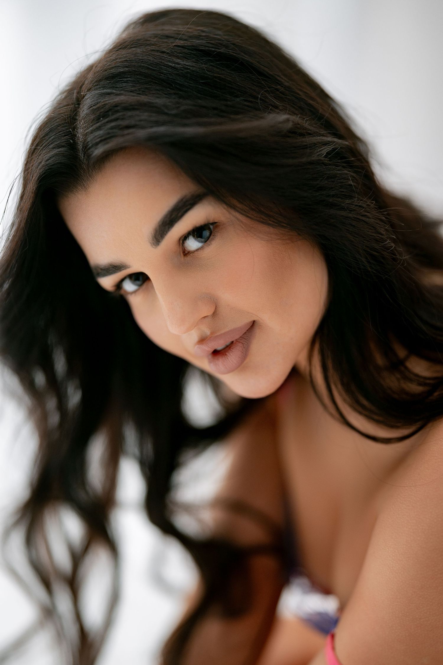 A portrait showcasing long dark hair and natural makeup against a soft white background.