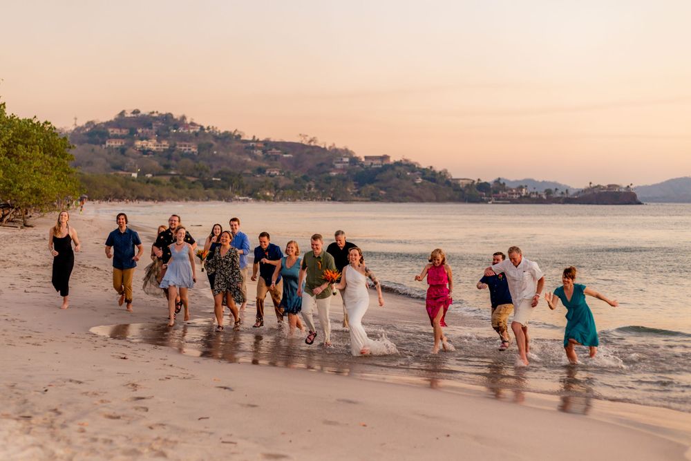 Large wedding party runs joyfully along tropical beach shoreline at golden sunset hour together. Guanacaste, Costa Rica