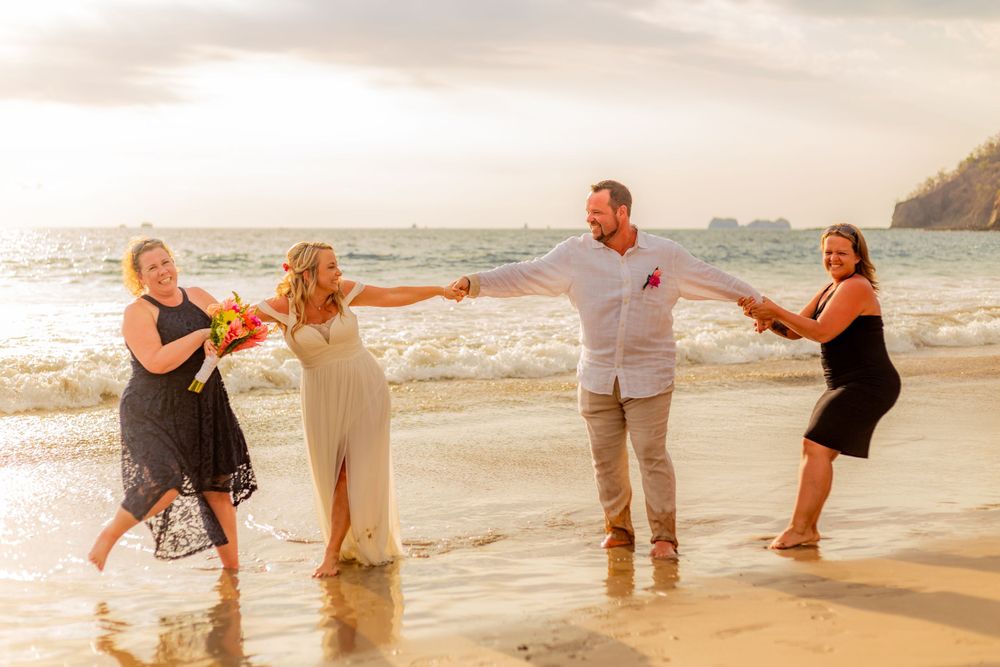 Bride and groom holding hands with two guests playfully splashing in ocean waves on a beach. Guanacaste, Costa Rica