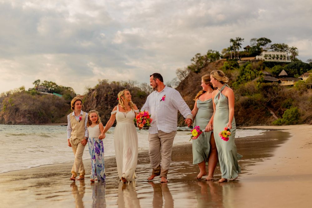 Wedding party walking along a tropical beach at sunset with lush green cliffs in the background. Guanacaste, Costa Rica