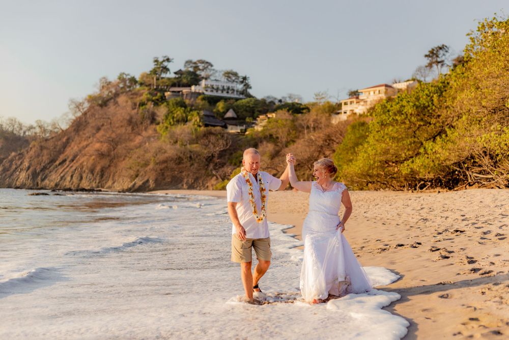 Joyful newlywed couple plays in ocean waves on sandy beach at sunset after wedding ceremony. Guanacaste, Costa Rica
