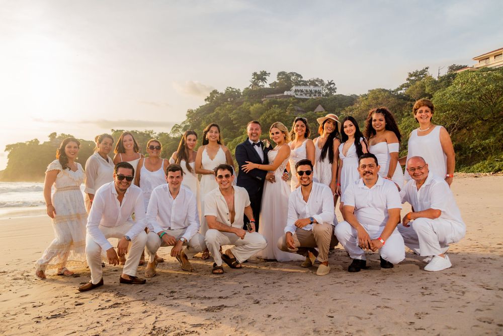 Large wedding party in white attire posing together on a tropical beach at golden hour sunset. Guanacaste, Costa Rica