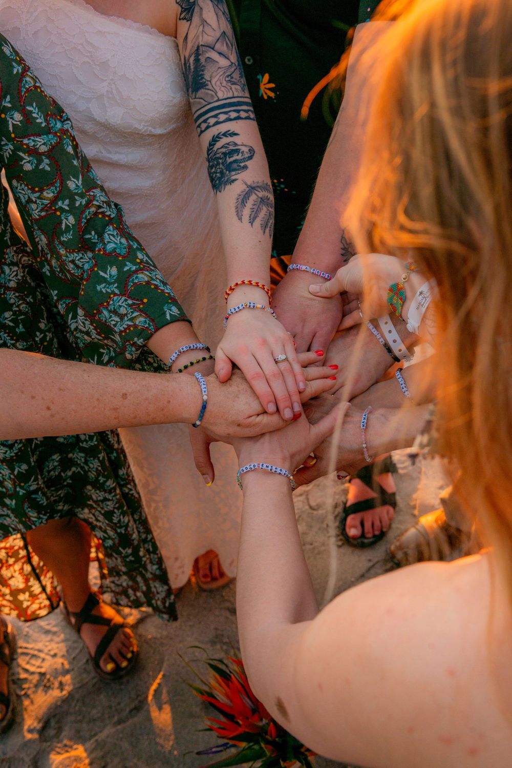 Wedding guests stack hands together showing matching bracelets and rings in a unity gesture outdoors. Guanacaste, Costa Rica