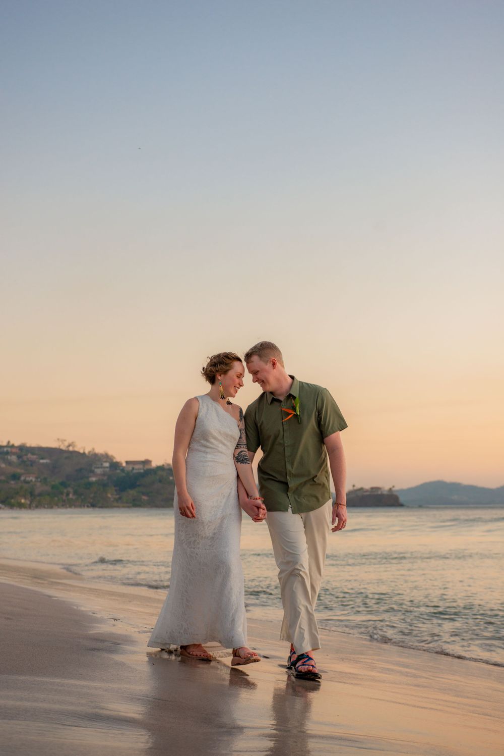 Newlywed couple walks hand in hand along beach shore at sunset after intimate wedding ceremony. Guanacaste, Costa Rica