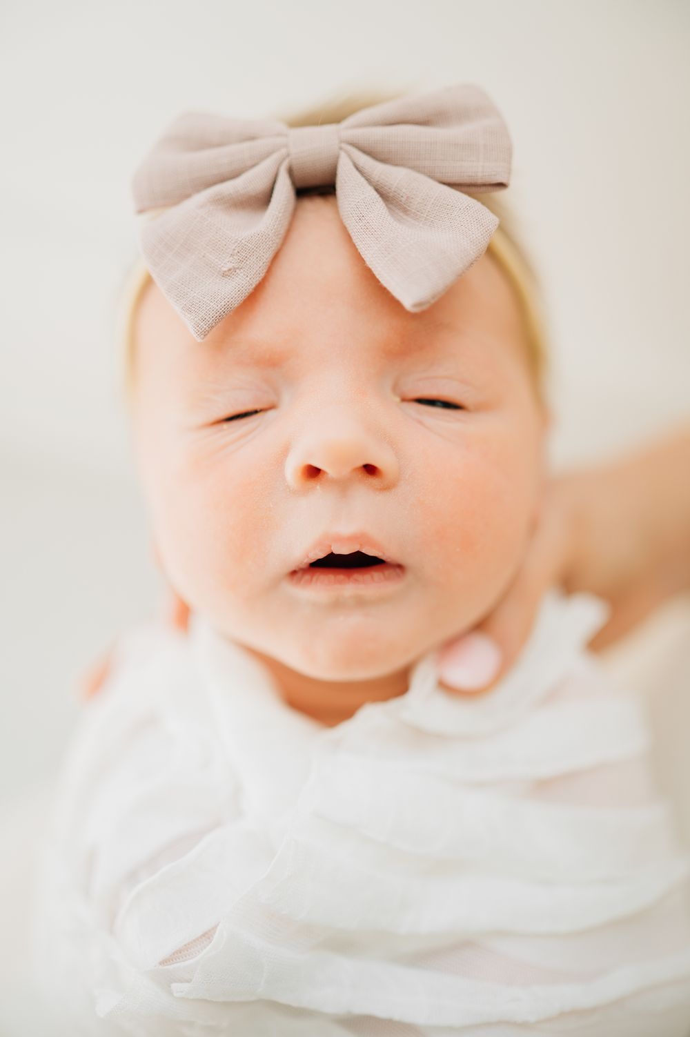 A sleeping baby wearing a light pink bow headband in a white outfit.