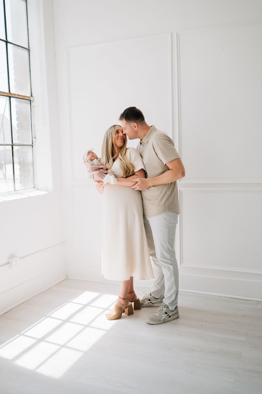 Family of three share tender moment in sunlit white room.
