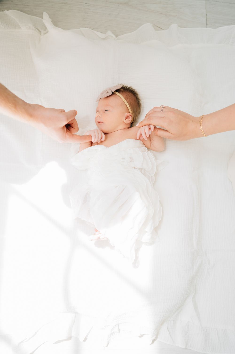 Overhead view of sleeping newborn on white blanket with parents' hands reaching in.